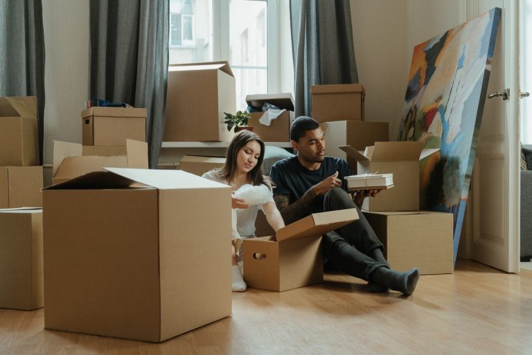 a couple sitting on the floor between a pile of cardboard boxes