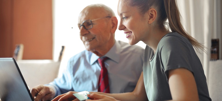 A woman and a senior preparing for a move by looking at a laptop and researching facilities, since that is one of the best ways to help seniors move