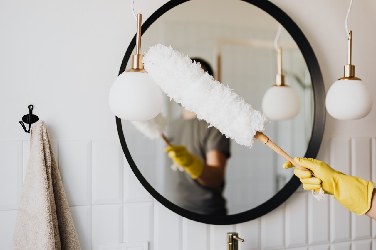 Hand in a rubber glove is cleaning mirror with duster.
