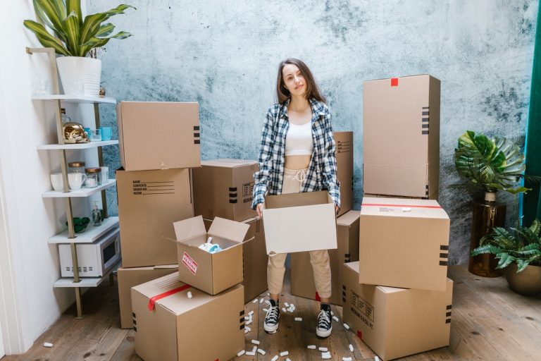 a woman holding a cardboard box while standing in between several cardboard boxes
