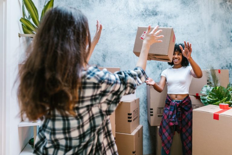 A woman throwing moving box to a friend.