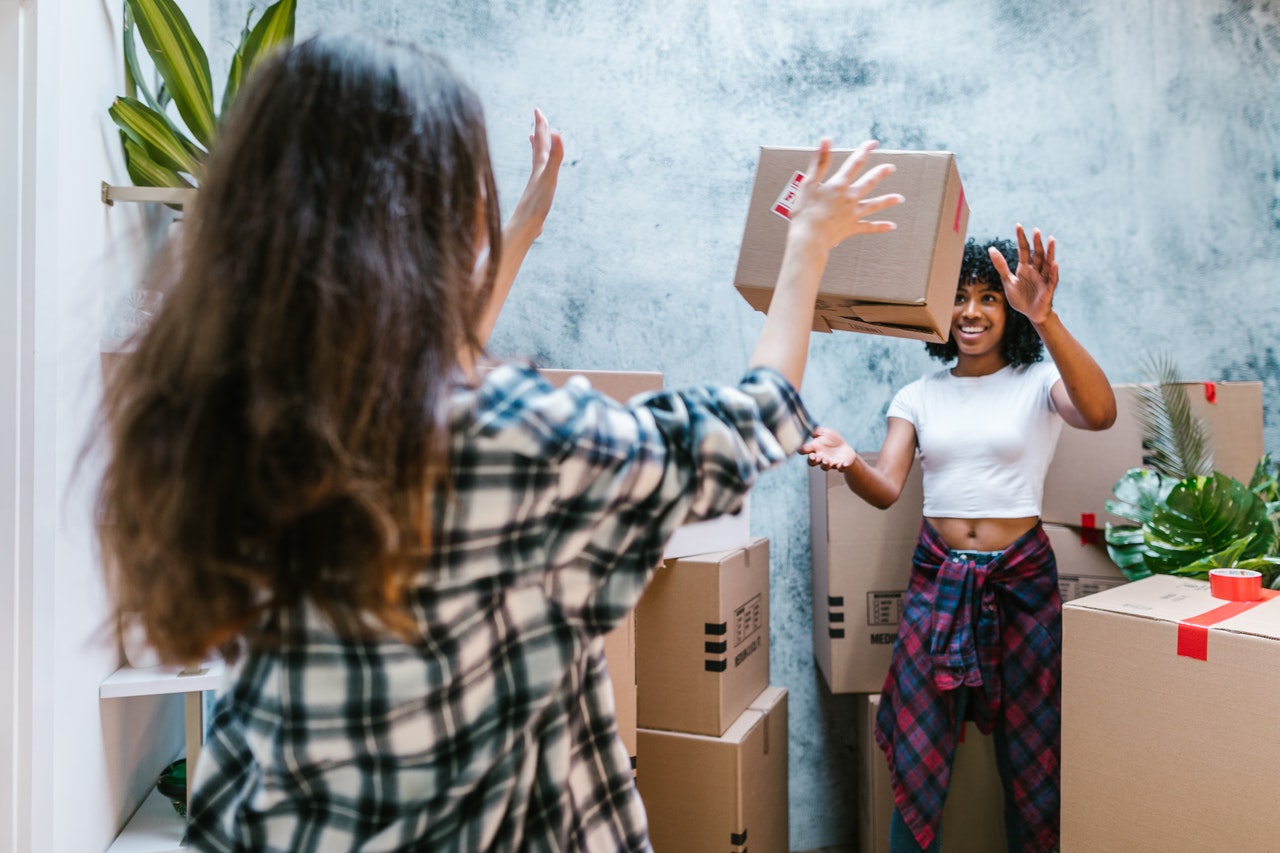 A woman throwing moving box to a friend.