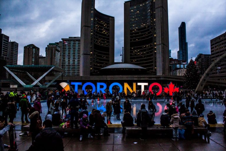 people standing in front of Toronto sign, surrounded by buildings