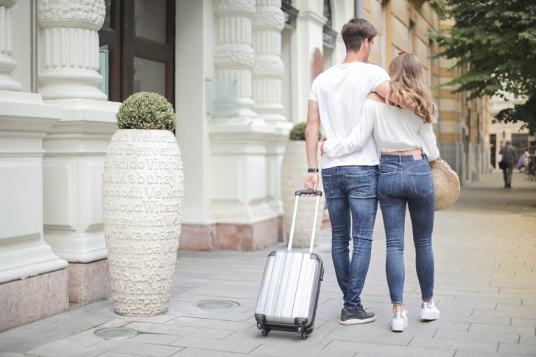 A couple holding each other and going somewhere with a suitcase.