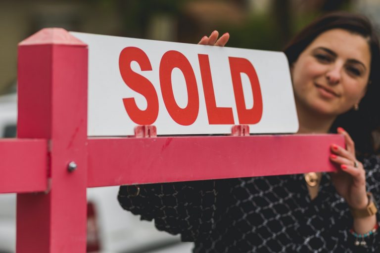 A woman putting a sold sign in front of a house