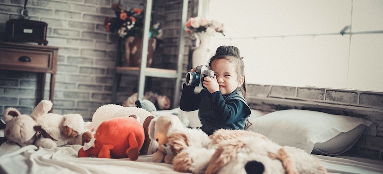 A girl surrounded by toys playing wit a camera
