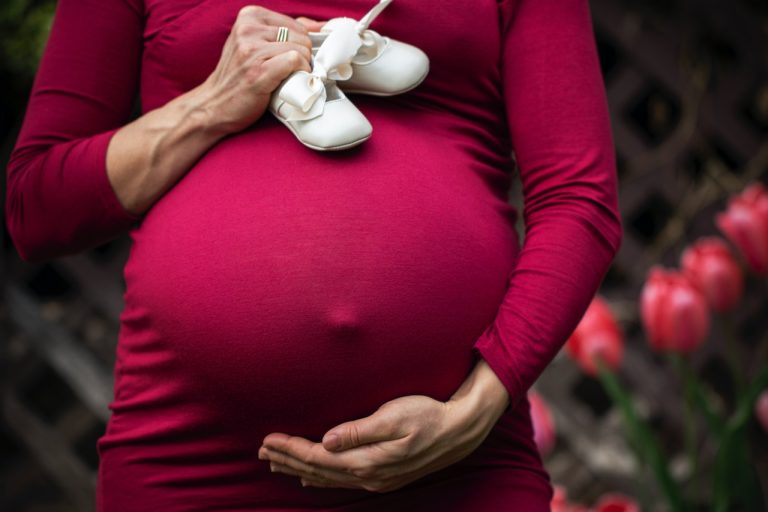 A woman in a red dress holding white baby shoes after moving safely in Canada while pregnant