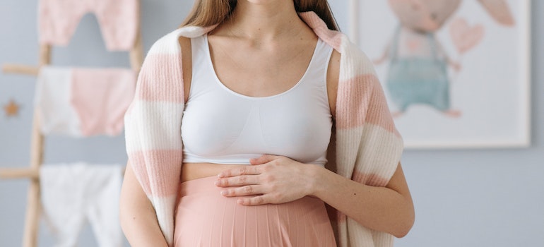 A woman in a kid's room, holding her stomach while pregnant