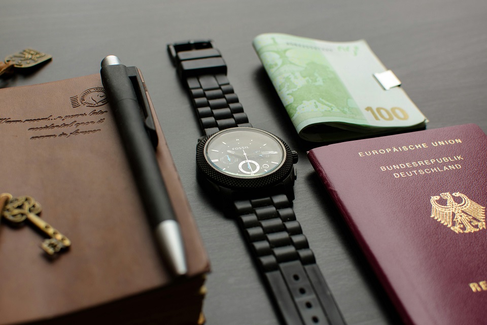 a watch, a passport and a notebook on a desk