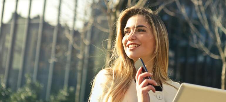 Woman using phone holding a tablet in sunlight.