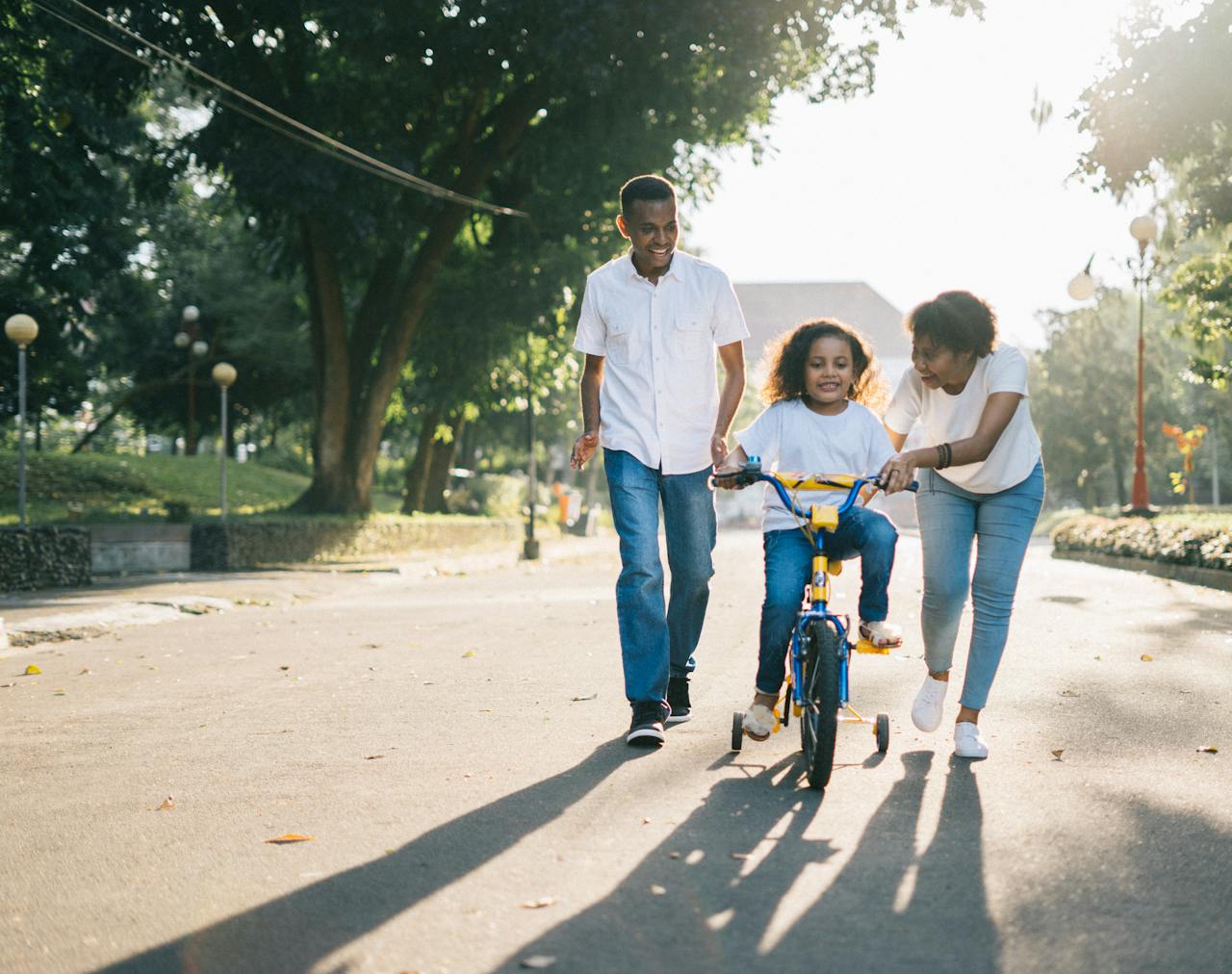 Parents helping child ride a bike in a family-friendly suburban neighborhood street.
